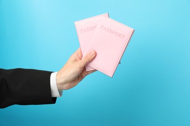 Photo of Woman holding passports in bright covers on light blue background, closeup