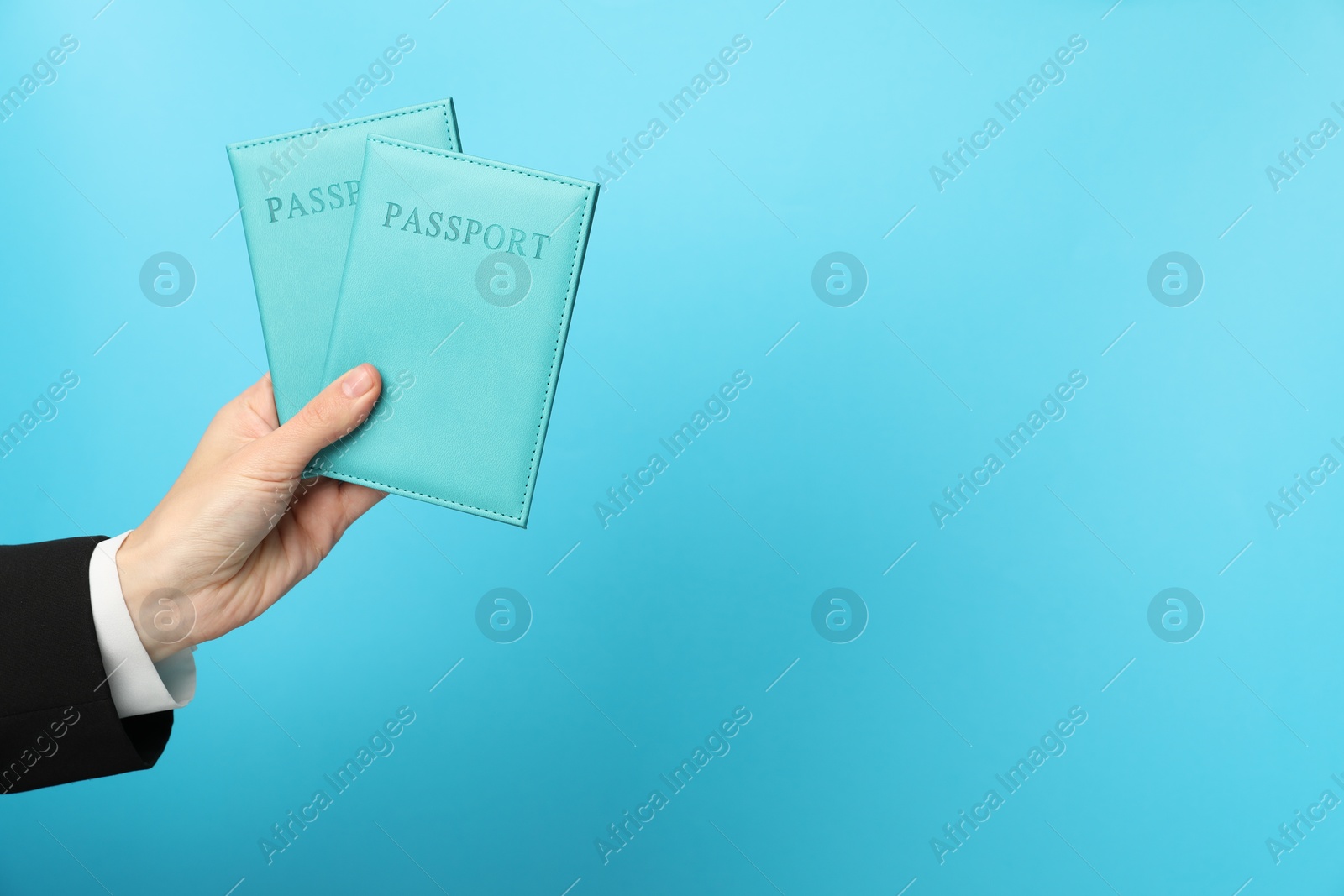 Photo of Woman holding passports in bright covers on light blue background, closeup. Space for text