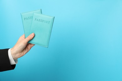 Photo of Woman holding passports in bright covers on light blue background, closeup. Space for text