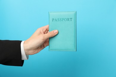 Photo of Woman holding passport in bright cover on light blue background, closeup