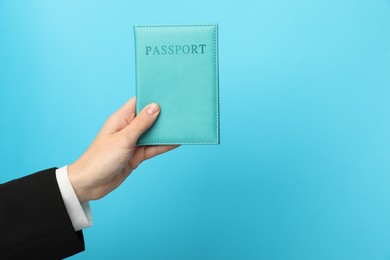 Photo of Woman holding passport in bright cover on light blue background, closeup. Space for text