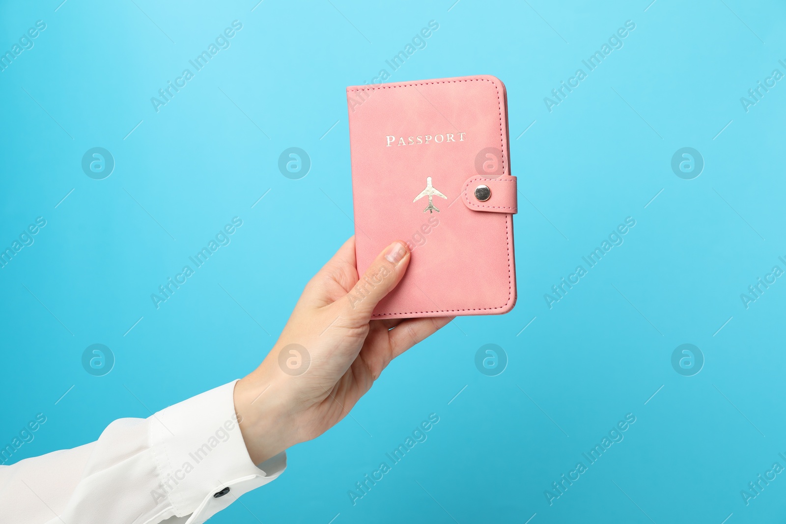 Photo of Woman holding passport in bright cover on light blue background, closeup