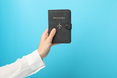 Woman holding passport in bright cover on light blue background, closeup