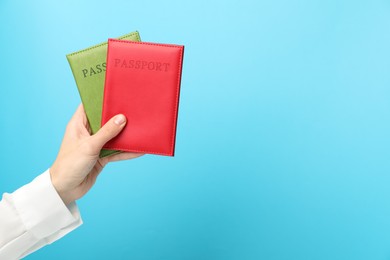 Photo of Woman holding passports in bright covers on light blue background, closeup. Space for text