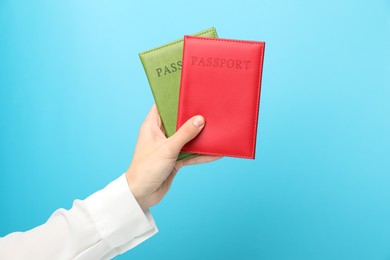 Photo of Woman holding passports in bright covers on light blue background, closeup