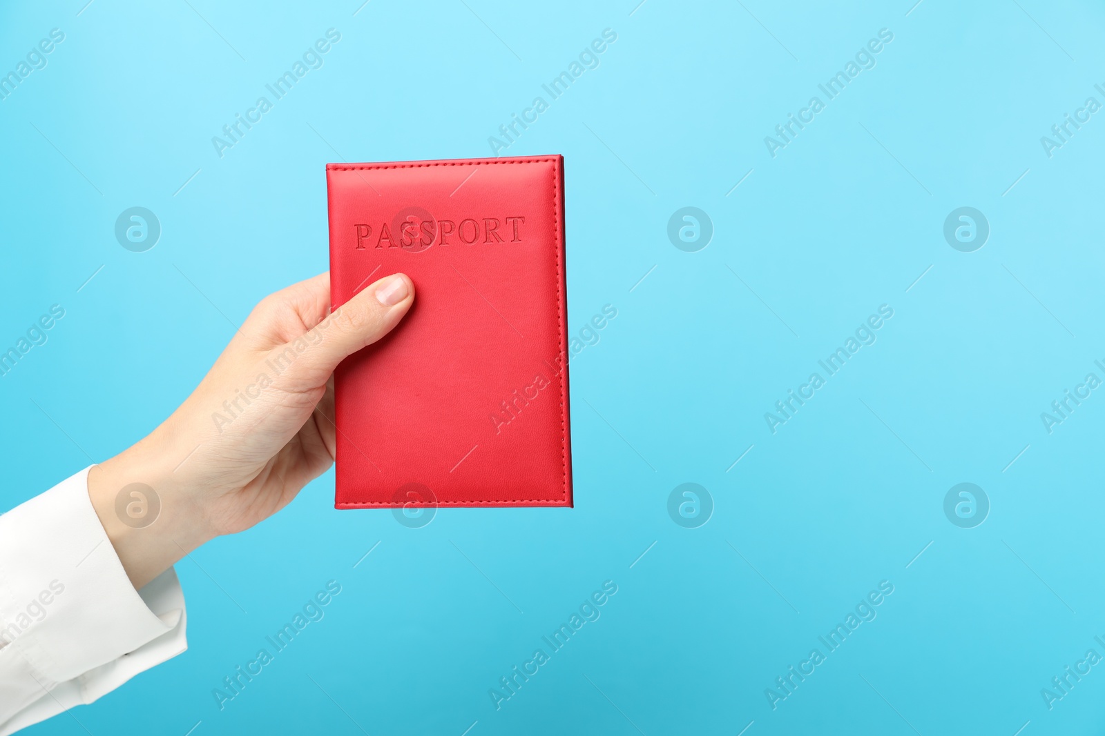 Photo of Woman holding passport in bright cover on light blue background, closeup. Space for text