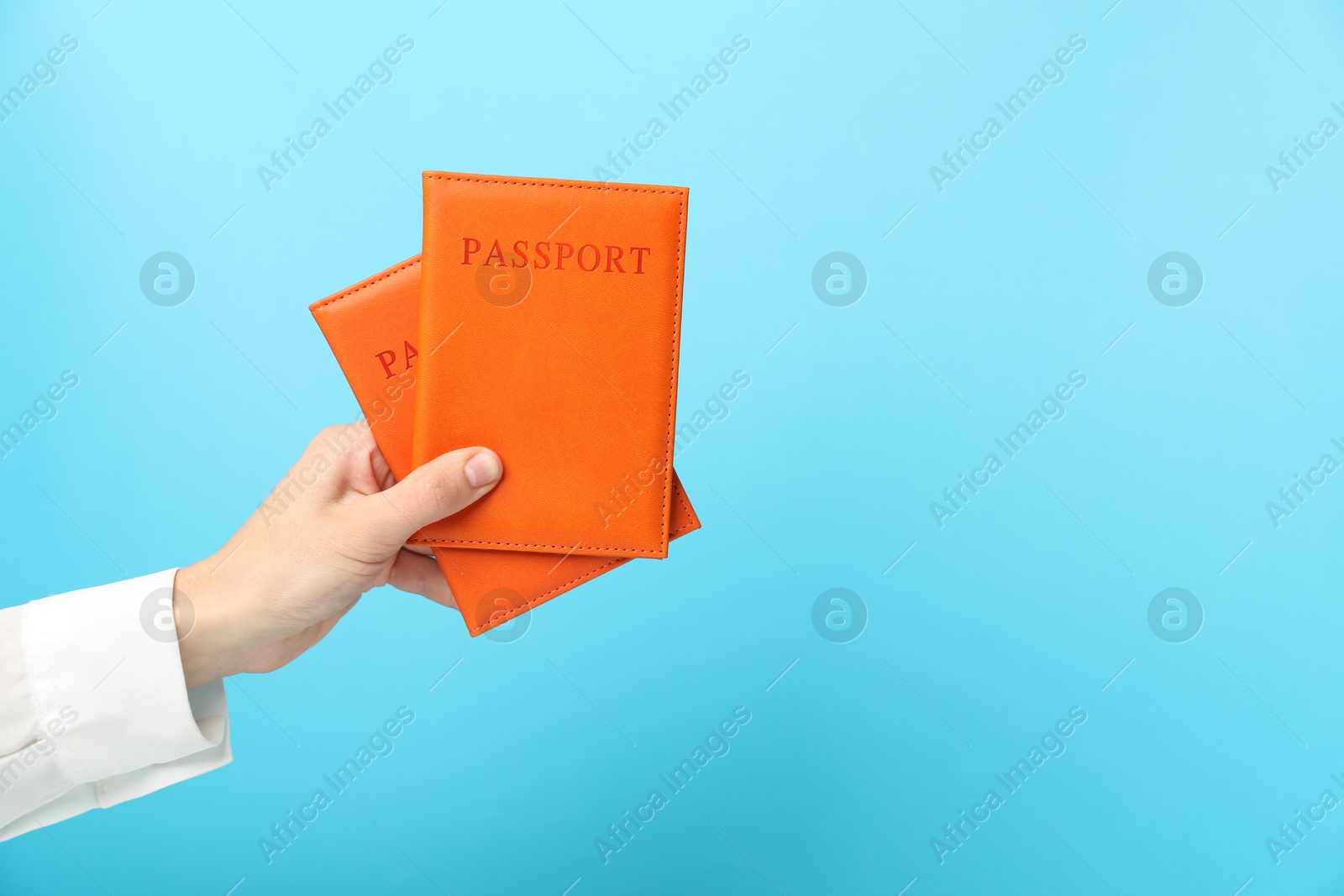 Photo of Woman holding passports in bright covers on light blue background, closeup. Space for text