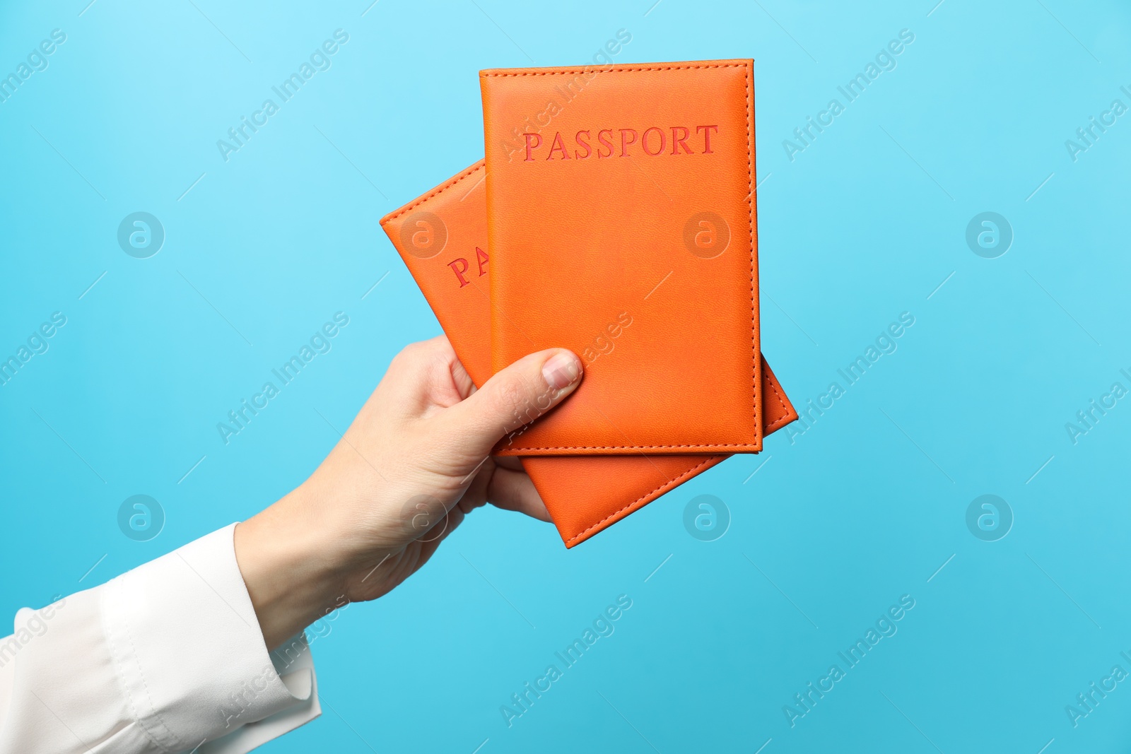 Photo of Woman holding passports in bright covers on light blue background, closeup