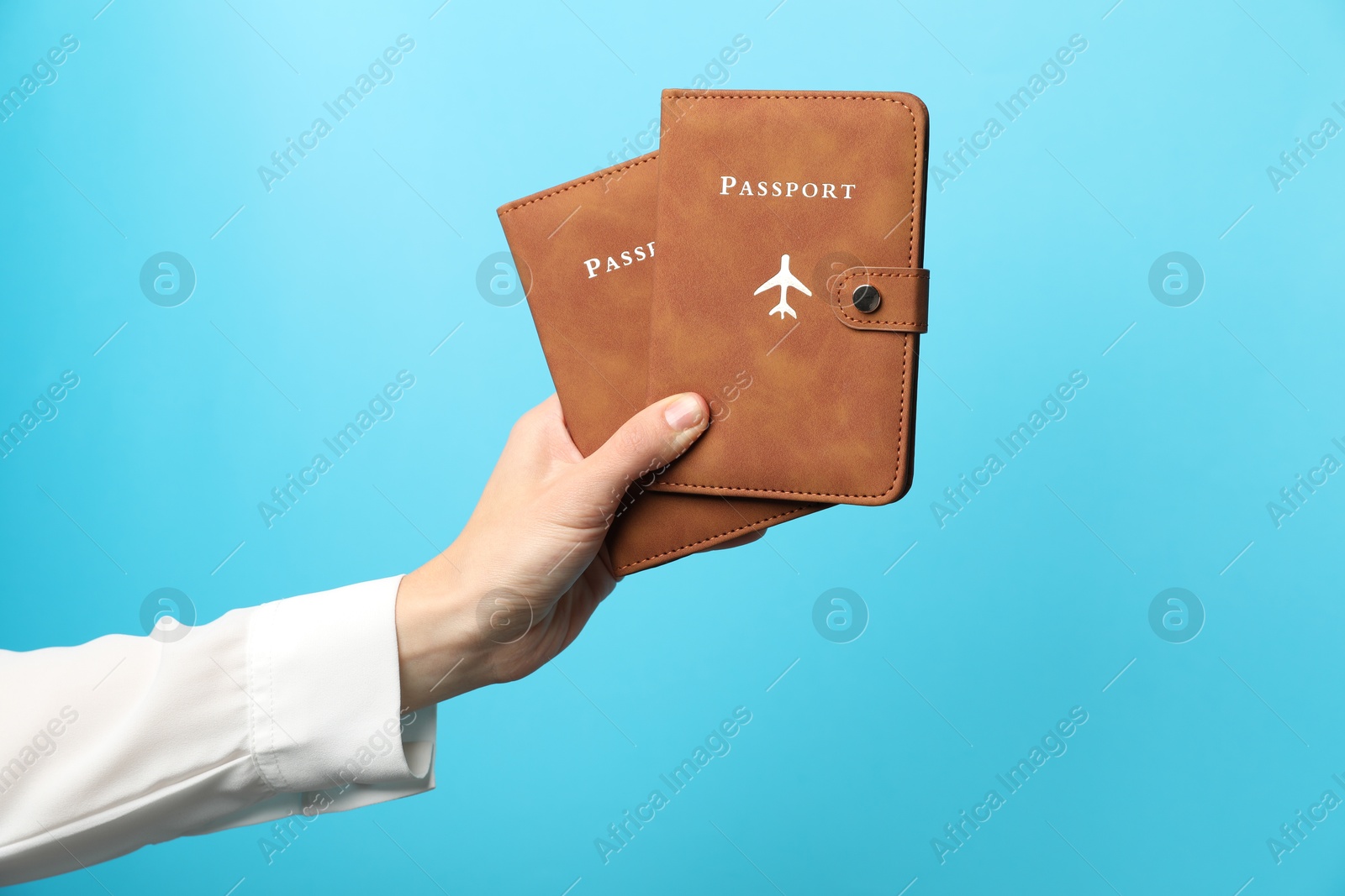 Photo of Woman holding passports in bright covers on light blue background, closeup