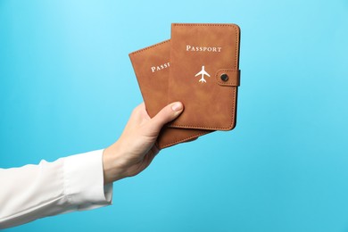 Photo of Woman holding passports in bright covers on light blue background, closeup