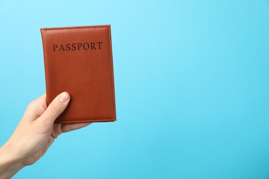 Photo of Woman holding passport in bright cover on light blue background, closeup. Space for text