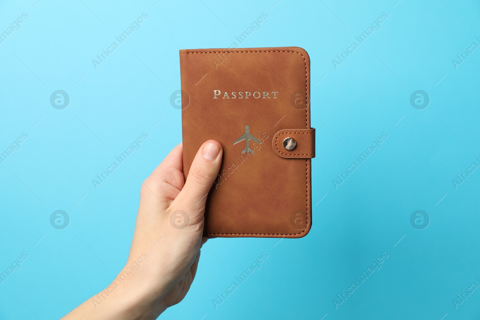 Photo of Woman holding passport in bright cover on light blue background, closeup