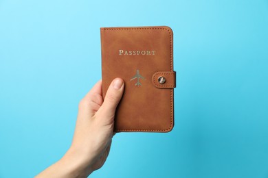 Photo of Woman holding passport in bright cover on light blue background, closeup