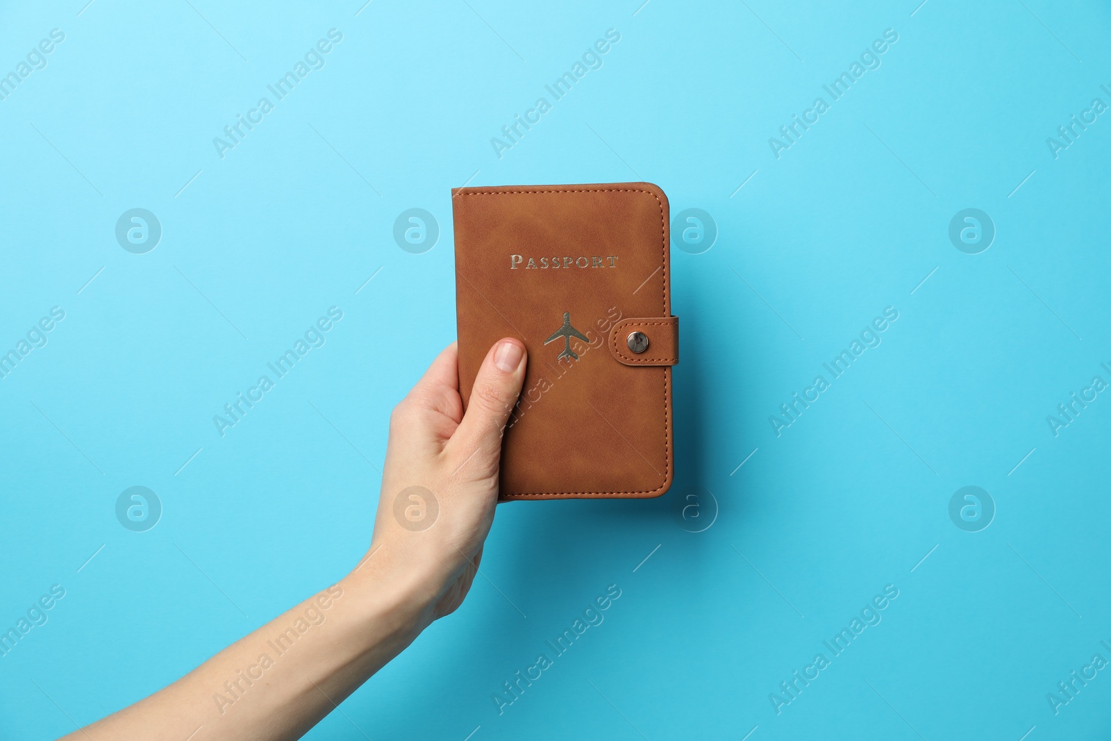 Photo of Woman holding passport in bright cover on light blue background, closeup