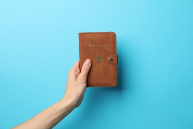 Photo of Woman holding passport in bright cover on light blue background, closeup