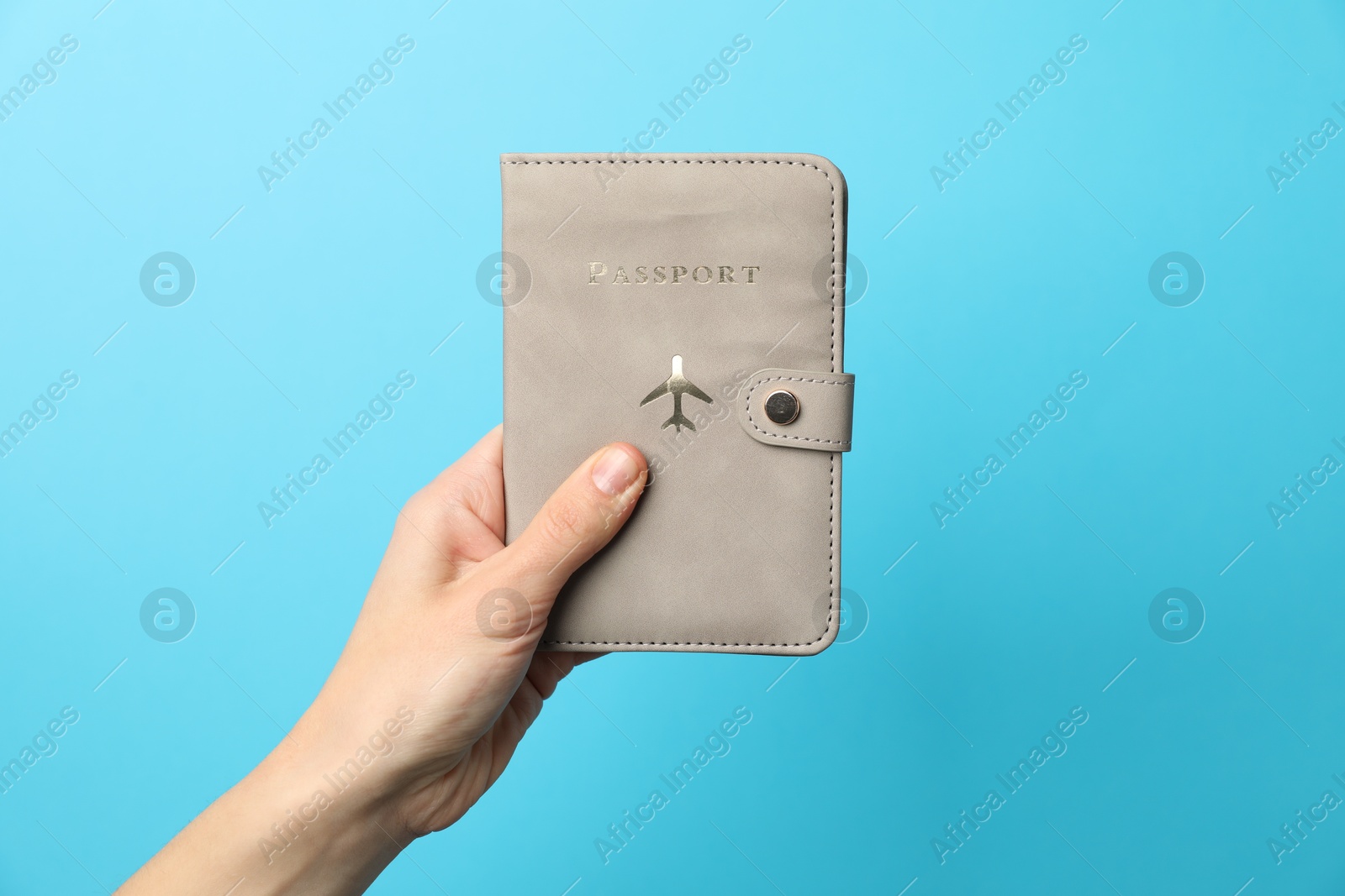 Photo of Woman holding passport in bright cover on light blue background, closeup