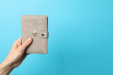 Photo of Woman holding passport in bright cover on light blue background, closeup. Space for text