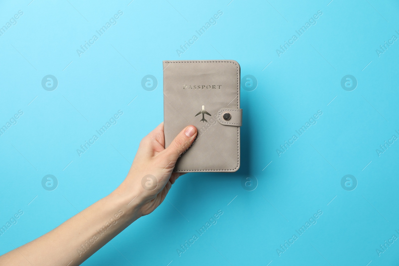 Photo of Woman holding passport in bright cover on light blue background, closeup