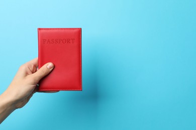 Photo of Woman holding passport in bright cover on light blue background, closeup. Space for text