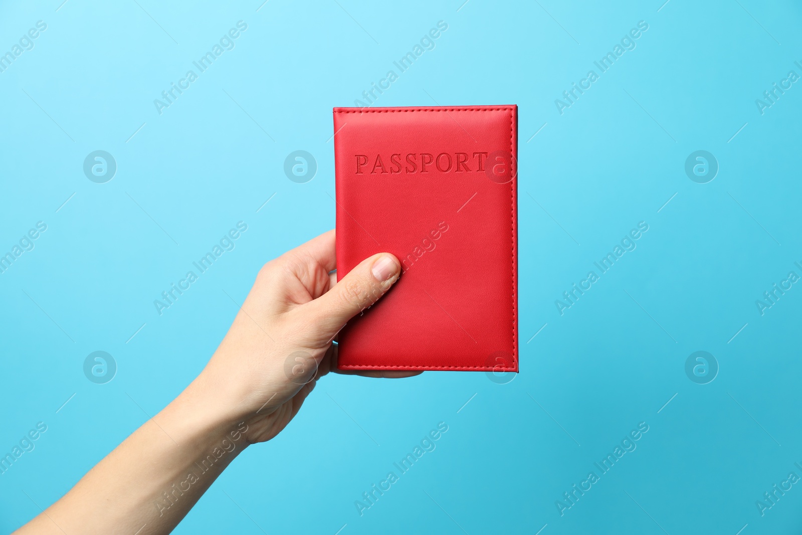 Photo of Woman holding passport in bright cover on light blue background, closeup