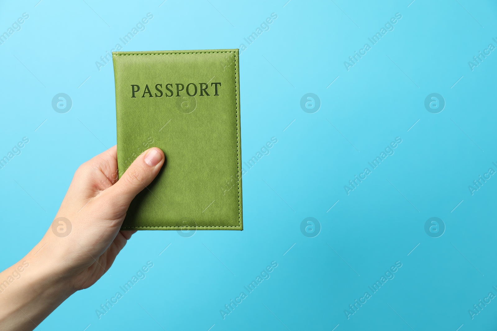 Photo of Woman holding passport in bright cover on light blue background, closeup. Space for text