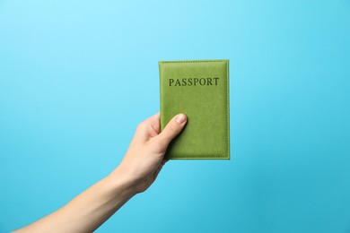 Photo of Woman holding passport in bright cover on light blue background, closeup