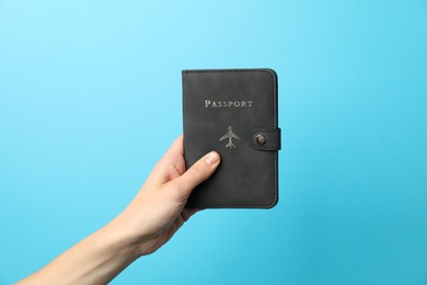 Photo of Woman holding passport in bright cover on light blue background, closeup