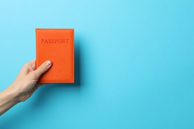 Photo of Woman holding passport in bright cover on light blue background, closeup. Space for text