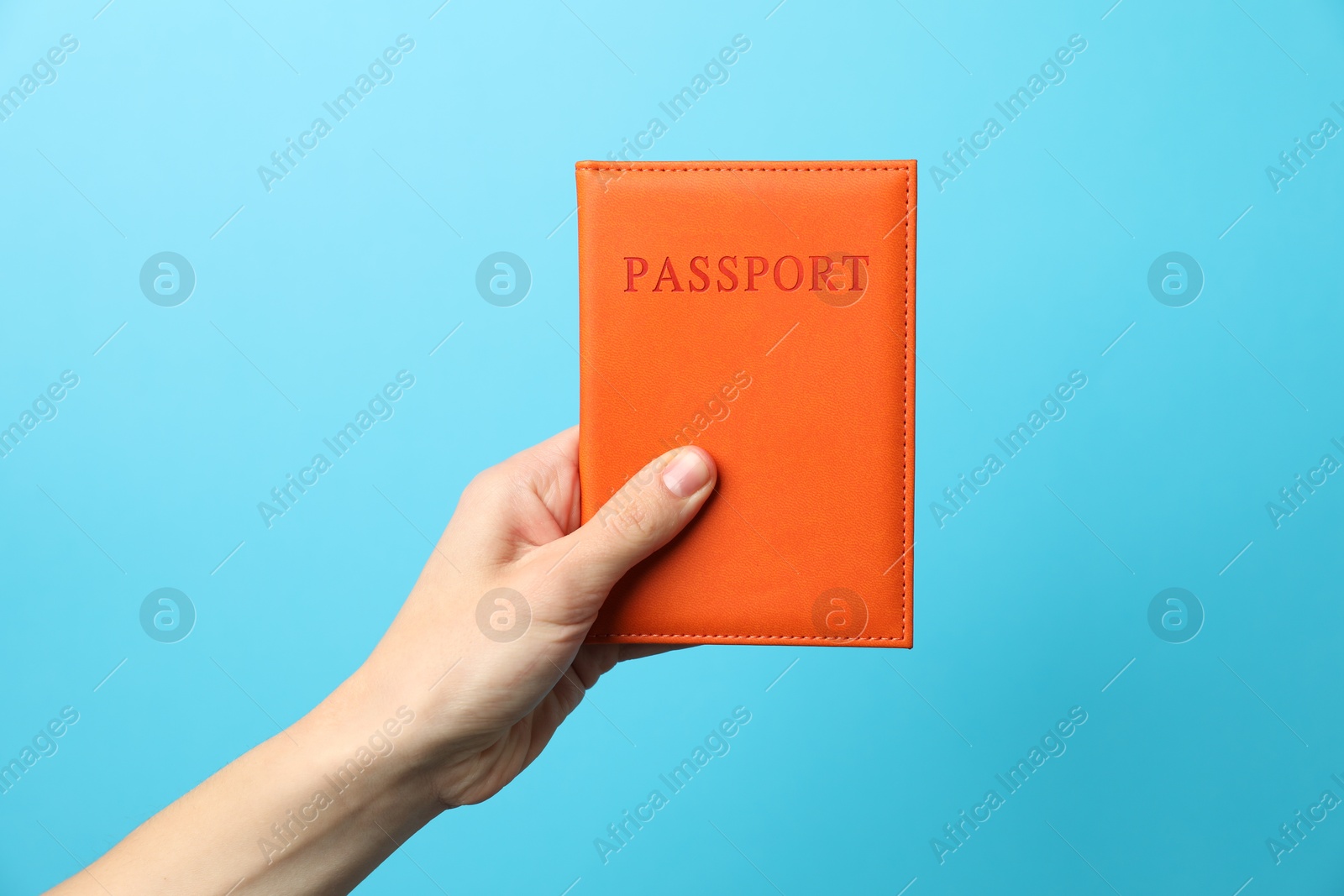 Photo of Woman holding passport in bright cover on light blue background, closeup