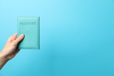 Photo of Woman holding passport in bright cover on light blue background, closeup. Space for text