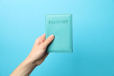 Photo of Woman holding passport in bright cover on light blue background, closeup