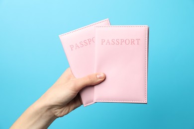 Photo of Woman holding passports in bright covers on light blue background, closeup