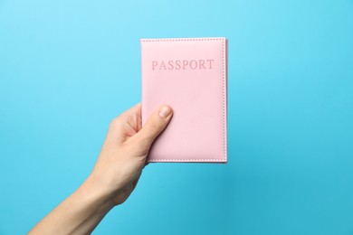 Photo of Woman holding passport in bright cover on light blue background, closeup