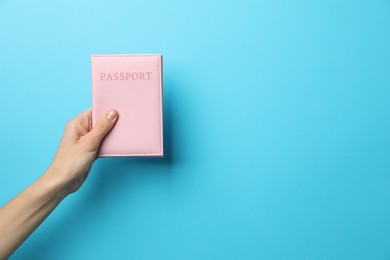 Photo of Woman holding passport in bright cover on light blue background, closeup. Space for text