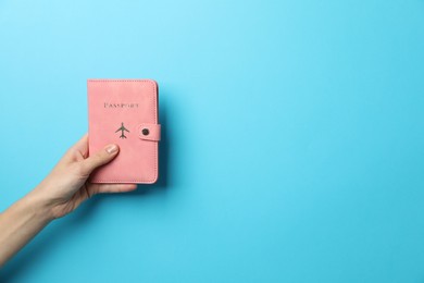 Photo of Woman holding passport in bright cover on light blue background, closeup. Space for text