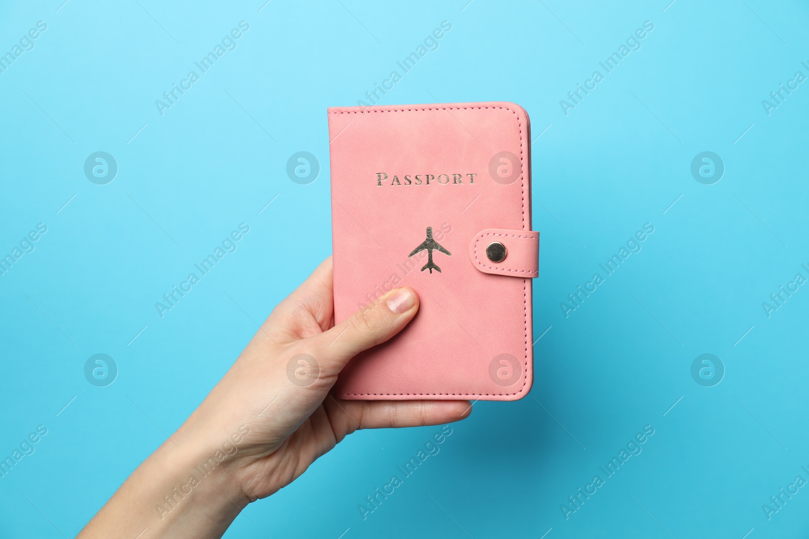 Photo of Woman holding passport in bright cover on light blue background, closeup