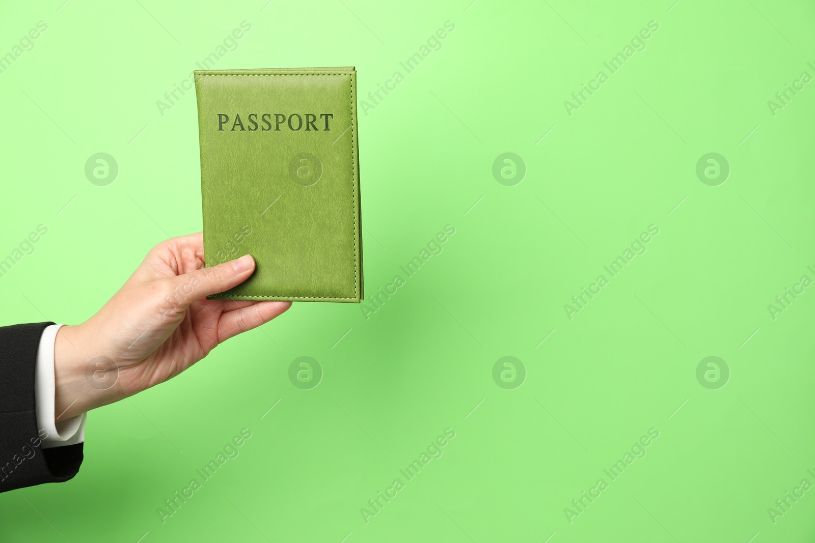 Photo of Woman holding passport in bright cover on green background, closeup. Space for text