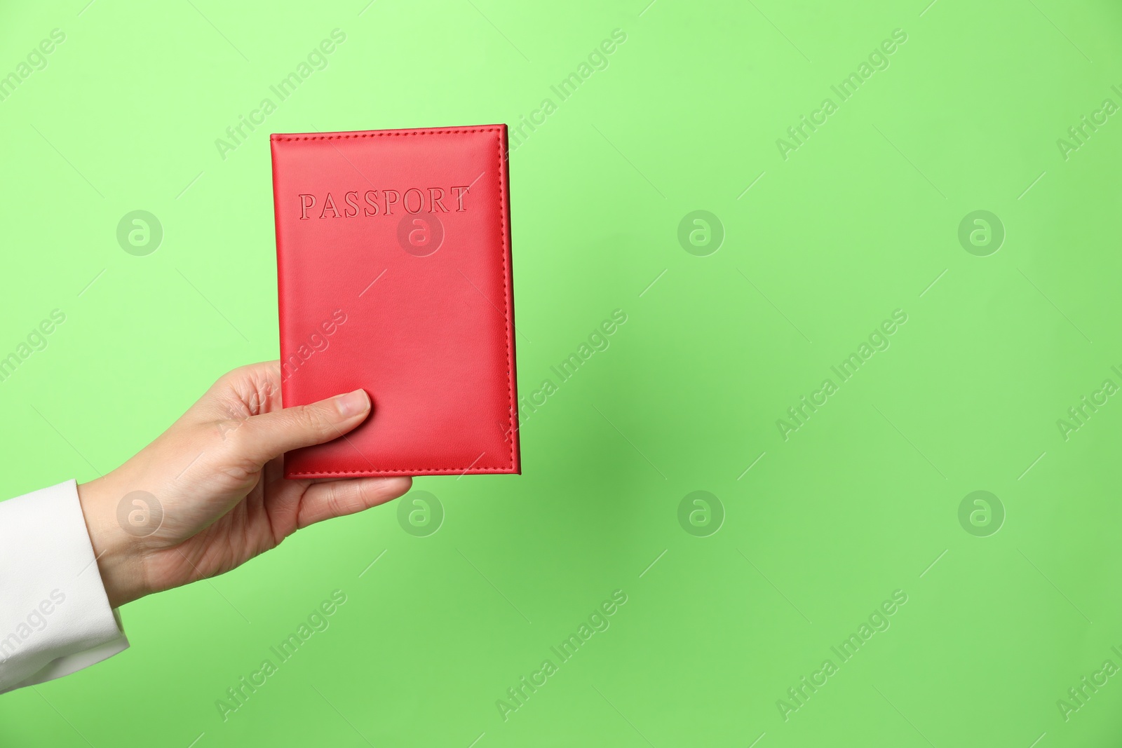 Photo of Woman holding passport in bright cover on green background, closeup. Space for text