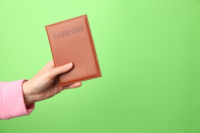 Photo of Woman holding passport in bright cover on green background, closeup. Space for text