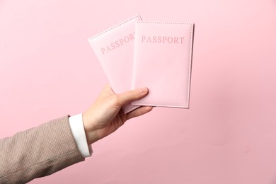 Photo of Woman holding passports in bright covers on pink background, closeup