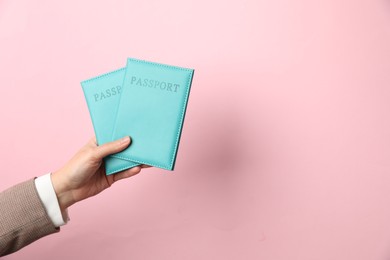 Photo of Woman holding passports in bright covers on pink background, closeup. Space for text