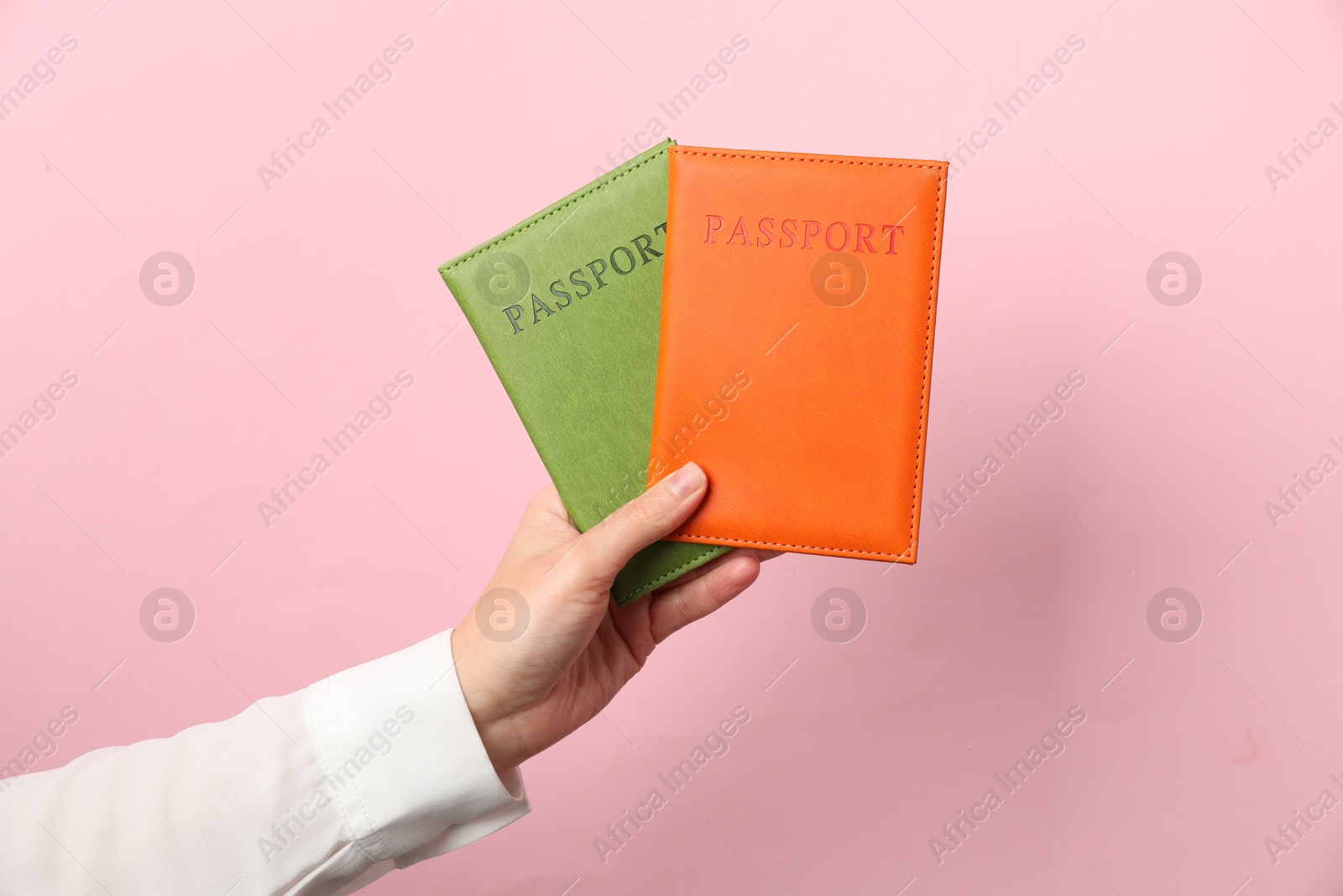 Photo of Woman holding passports in bright covers on pink background, closeup