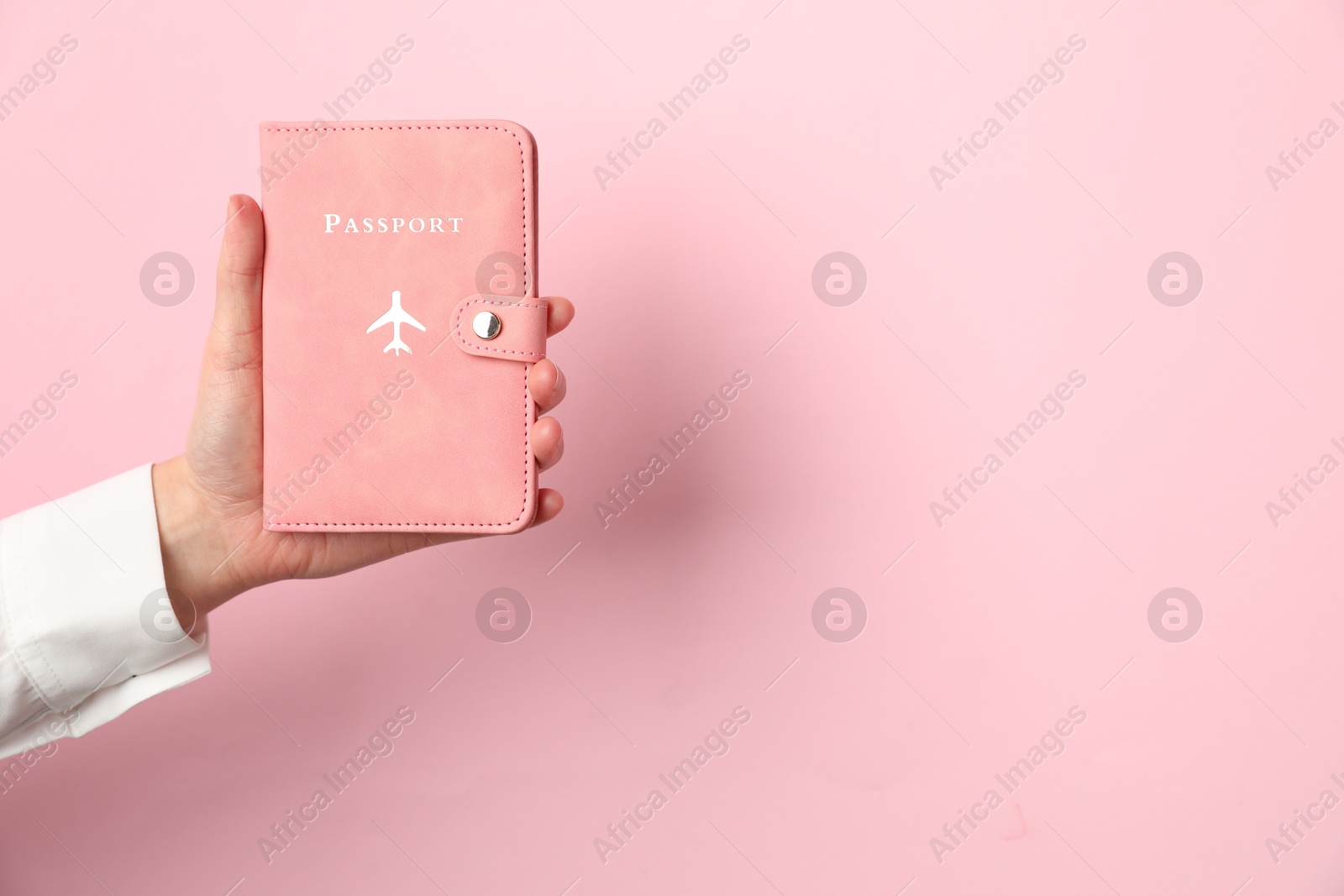 Photo of Woman holding passport in bright cover on pink background, closeup. Space for text