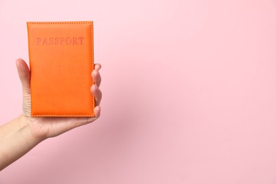 Photo of Woman holding passport in bright cover on pink background, closeup. Space for text