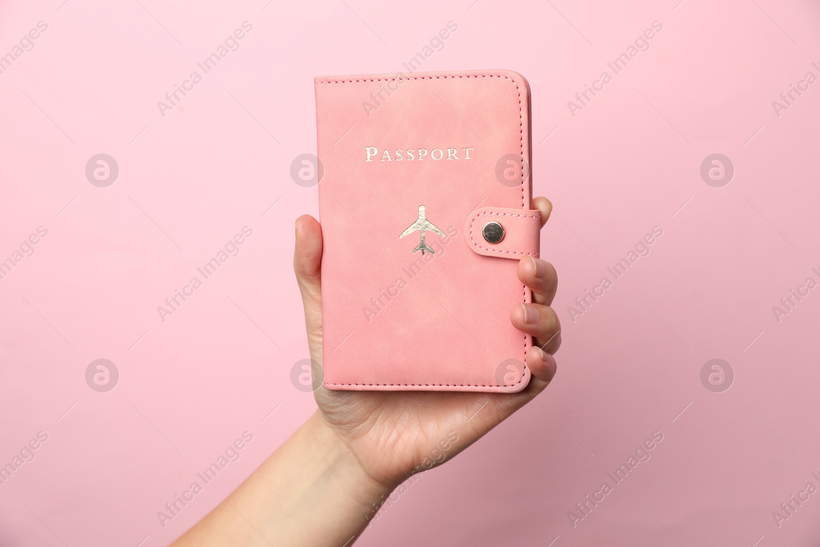 Photo of Woman holding passport in bright cover on pink background, closeup