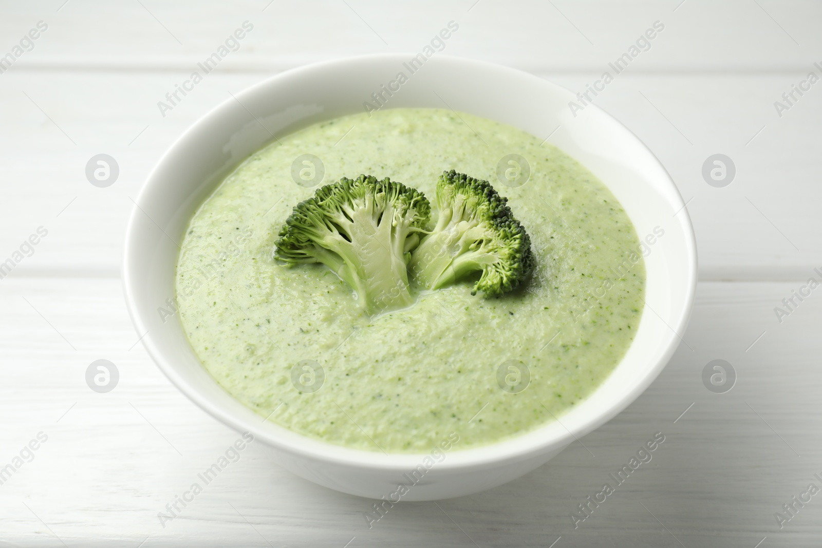 Photo of Delicious broccoli cream soup in bowl on white wooden table, closeup