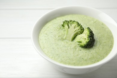 Photo of Delicious broccoli cream soup in bowl on white wooden table, closeup