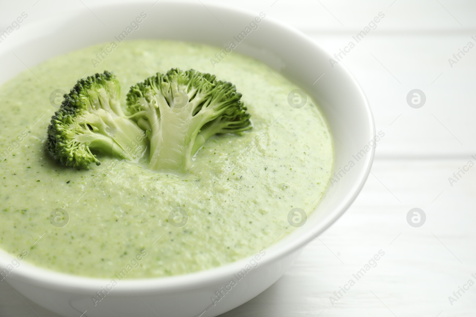 Photo of Delicious broccoli cream soup in bowl on white wooden table, closeup