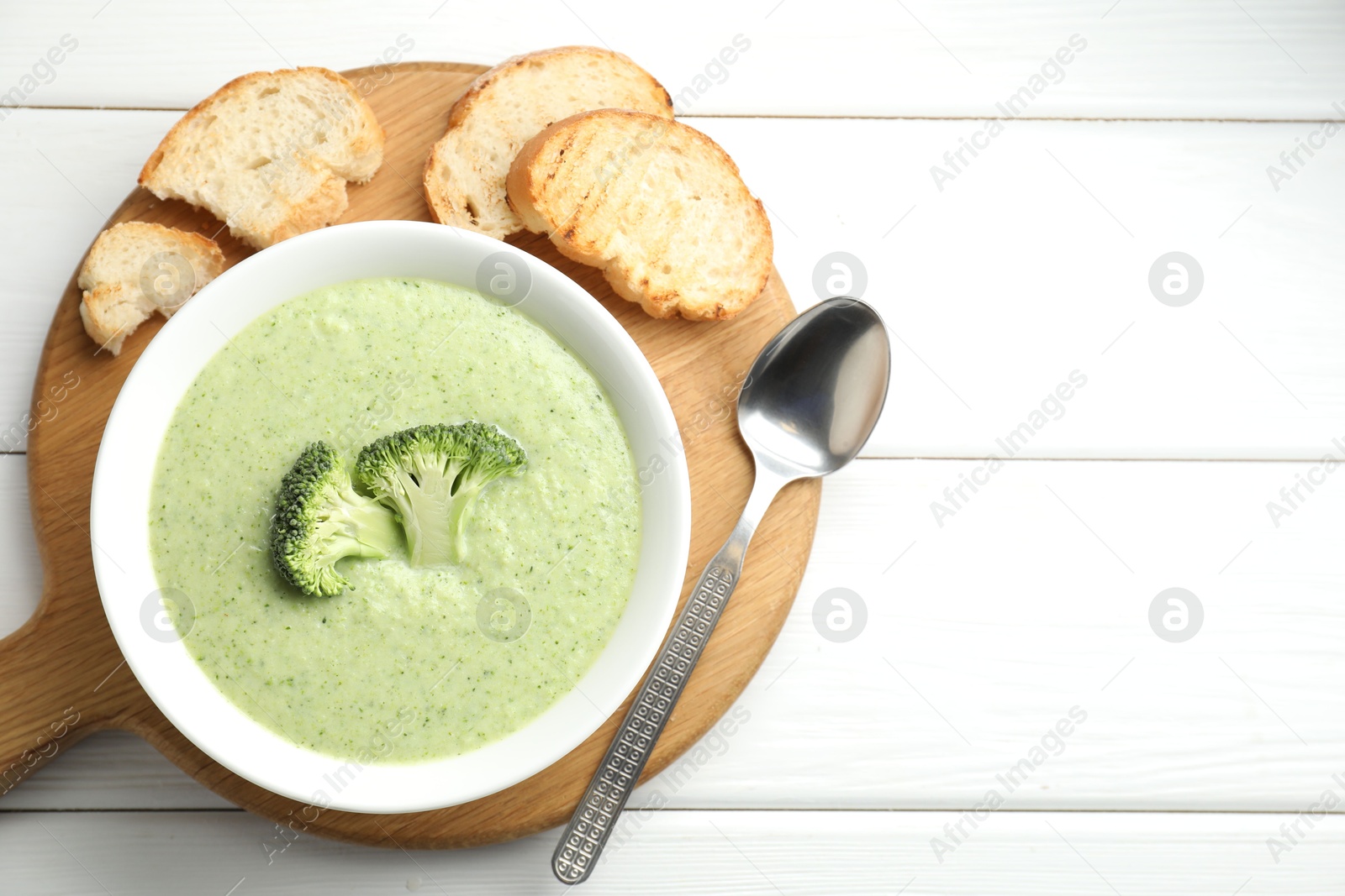 Photo of Delicious broccoli cream soup served on white wooden table, top view. Space for text