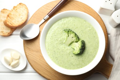 Photo of Delicious broccoli cream soup served on white wooden table, flat lay